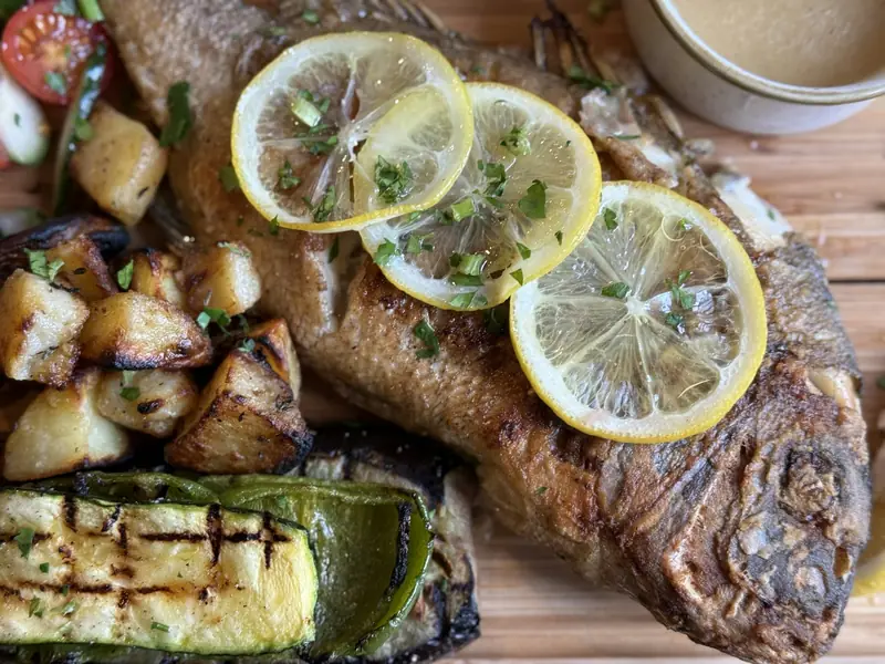 Pescado entero a la brasa con rodajas de limón y verduras